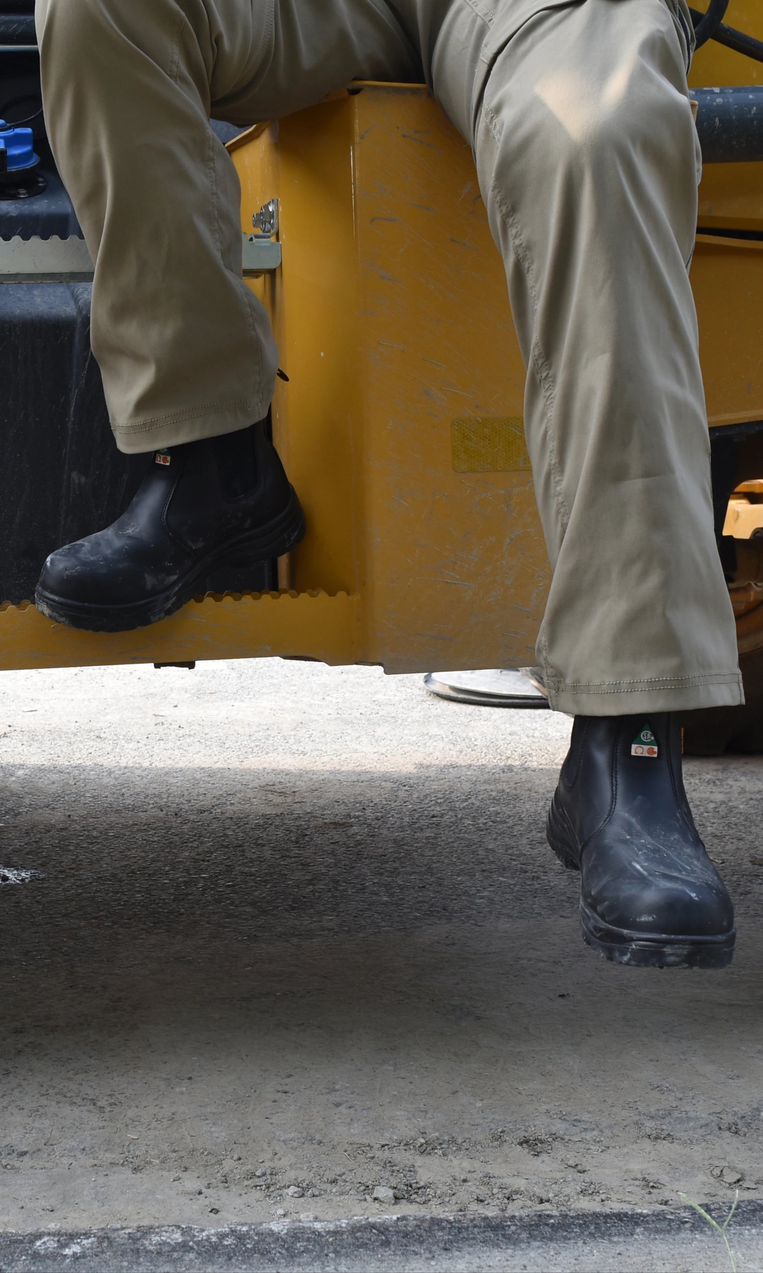 Person wearing black boots and beige pants sitting on a yellow construction vehicle.