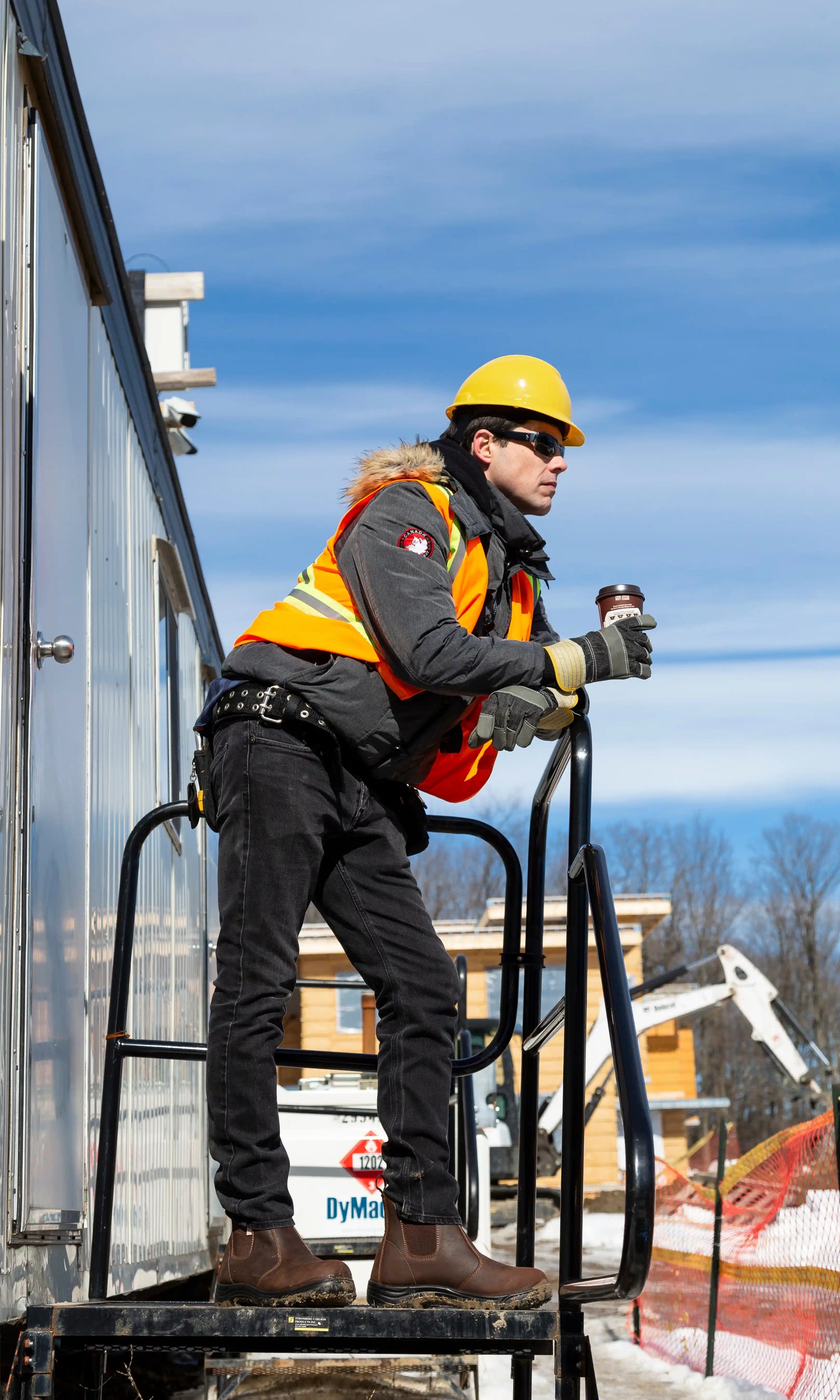 PPE man resting wearing safety boots and holding a coffee at a construction site
