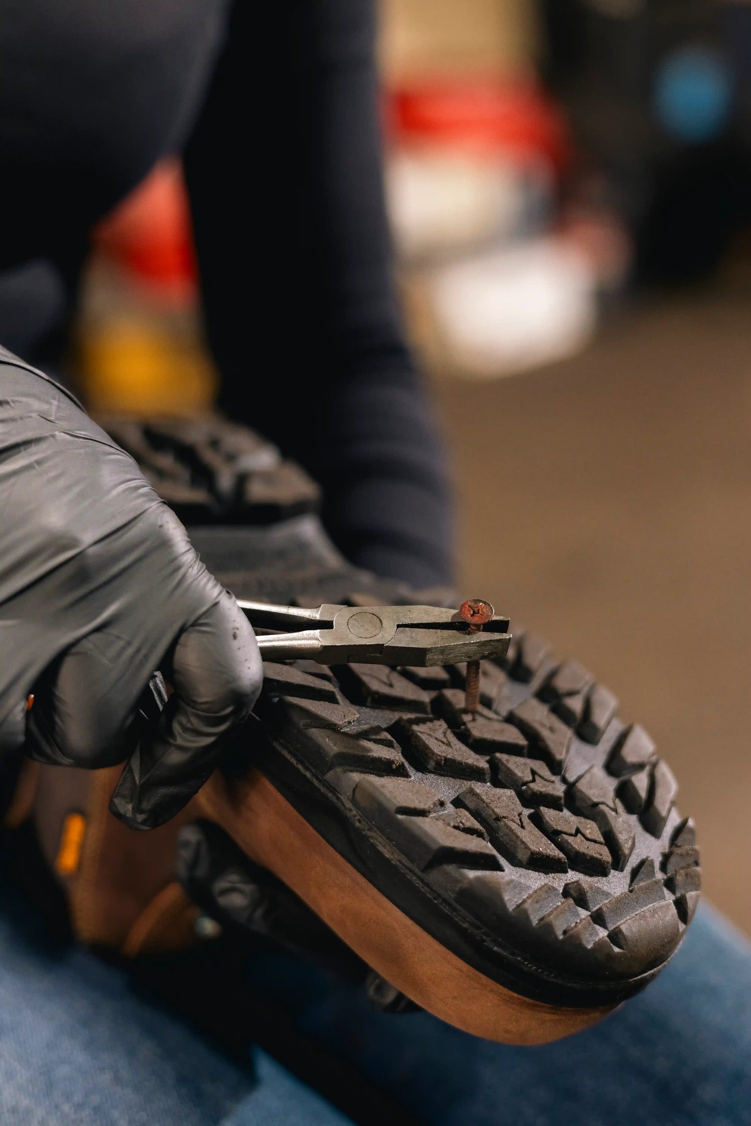 Woman wearing a glove and using pliers on a nail in the outsole
