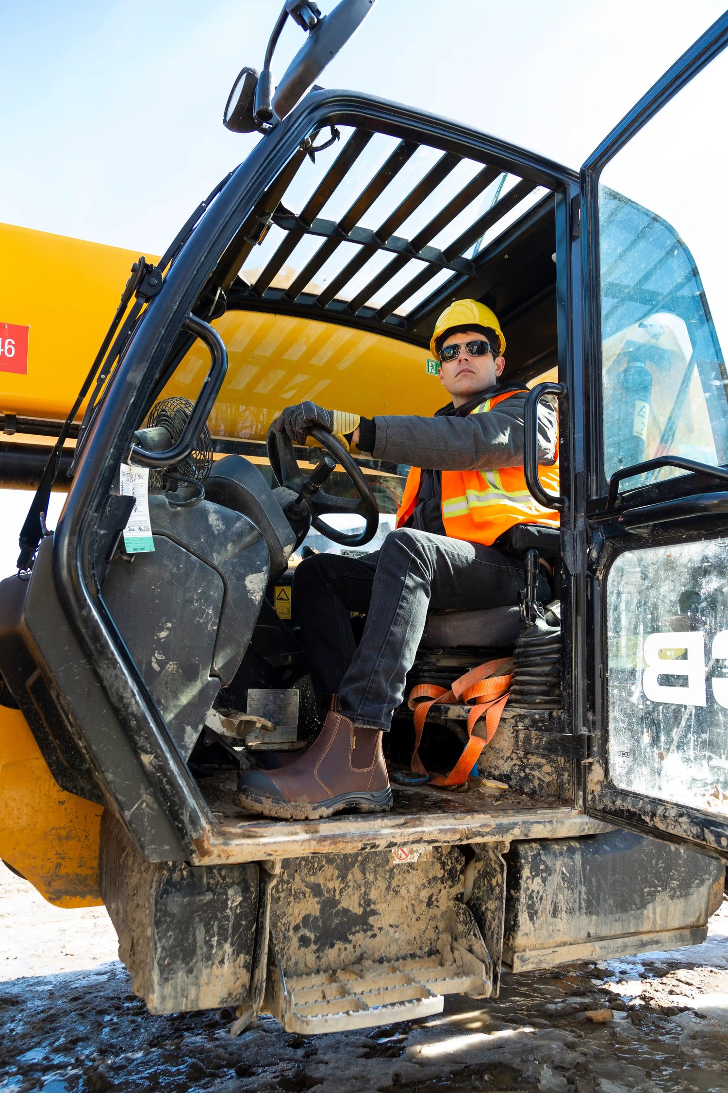 Person operating a yellow construction vehicle on a clear day wearing steel toe boots