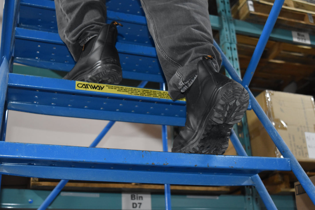 Composite toe work boots on a person climbing blue industrial stairs in a warehouse