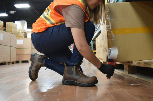 Warehouse worker taping boxes, wearing composite toe work boots and safety vest