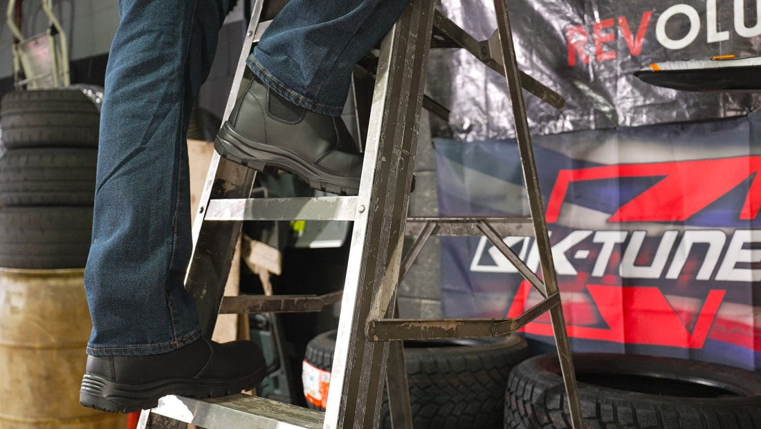 Close-up of person wearing black composite toe work boots on ladder in industrial garage