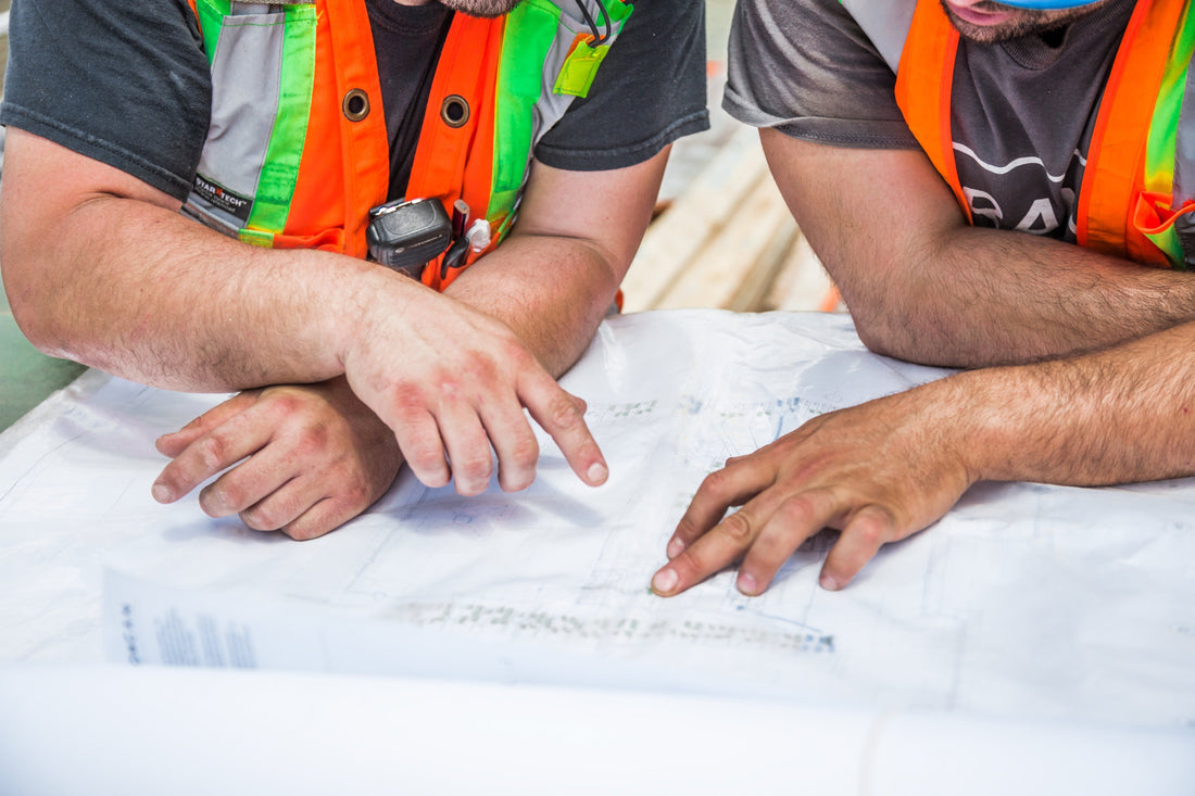 Construction workers in safety vests reviewing blueprints on site