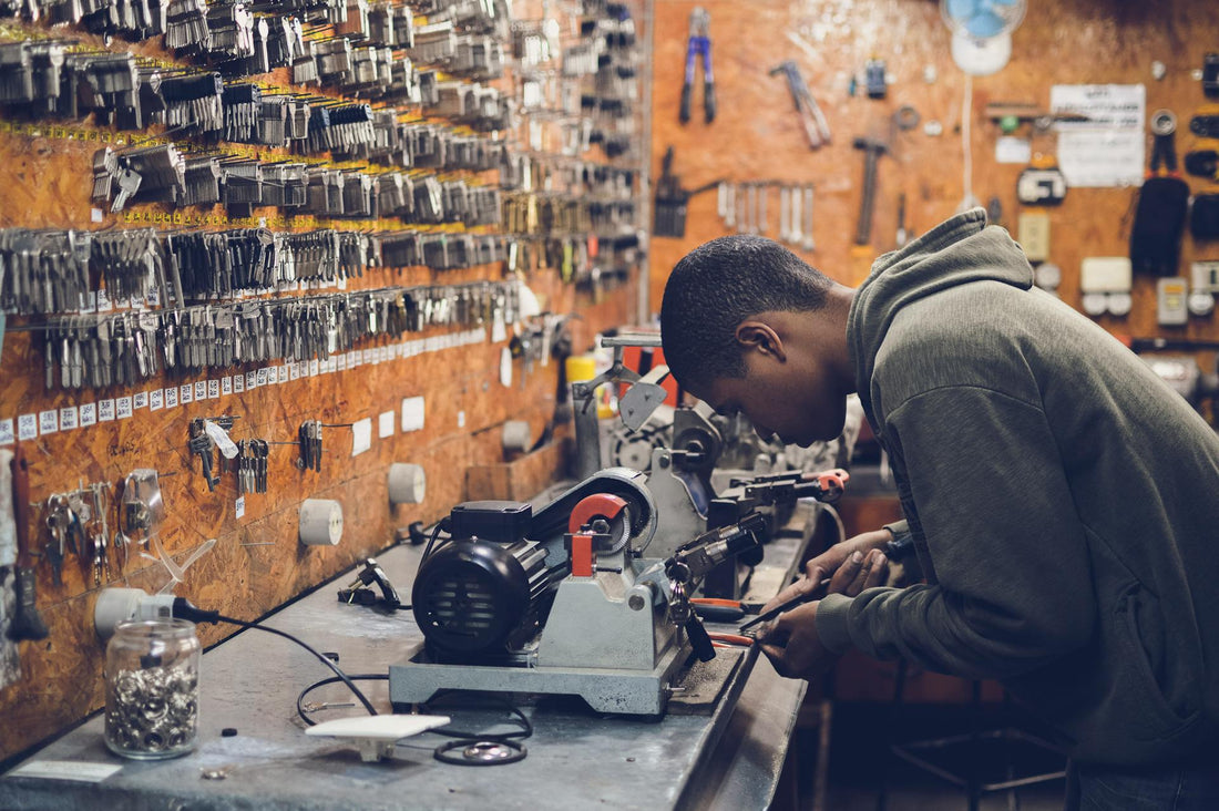Man working at key cutting machine in industrial locksmith workshop with tools and keys