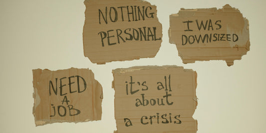 Cardboard signs with handwritten messages about job loss and needing employment on a neutral background.