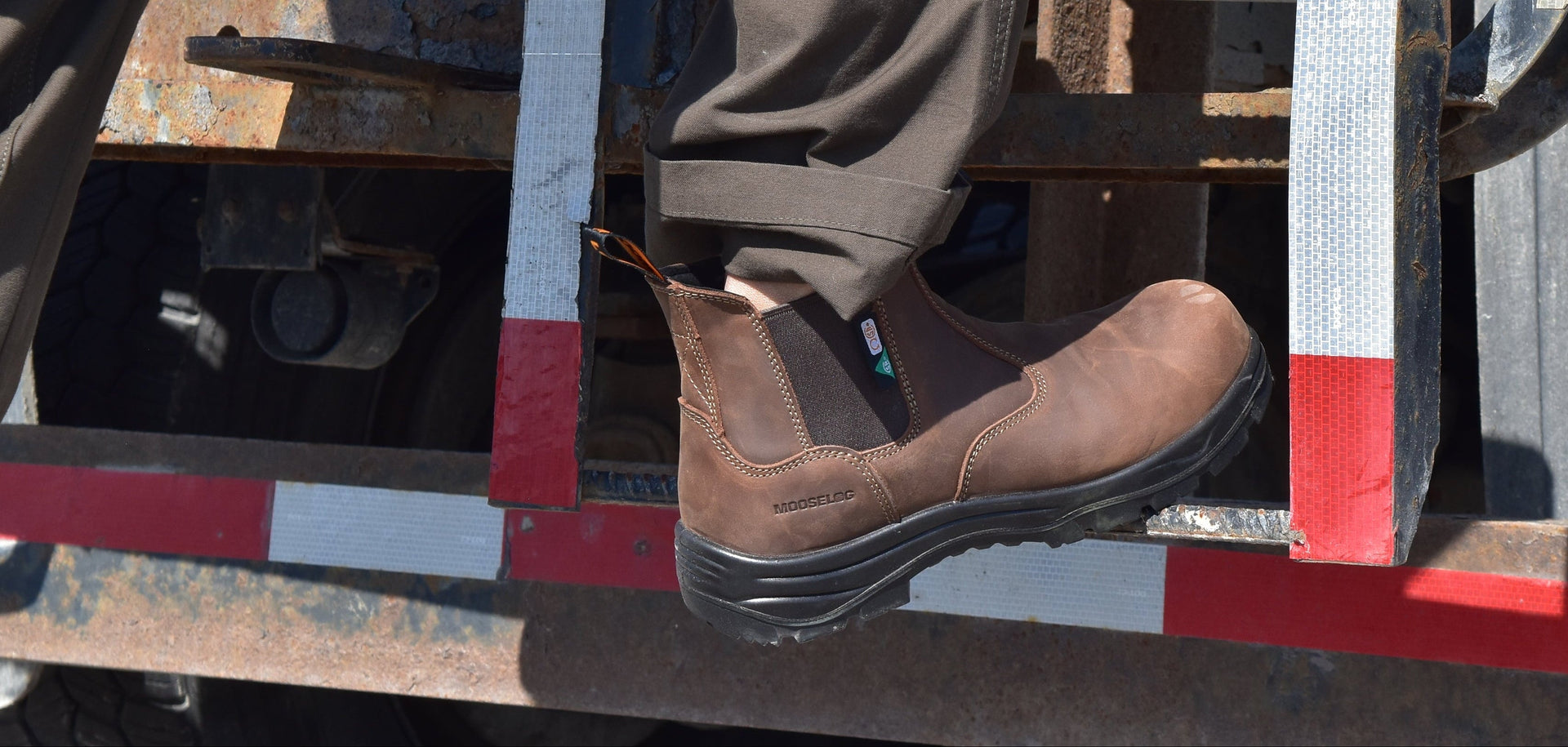 A person wearing brown slip-on work boots and dark pants steps onto the metal ladder of a truck, with the truck bed and Ontario license plate visible in the background.