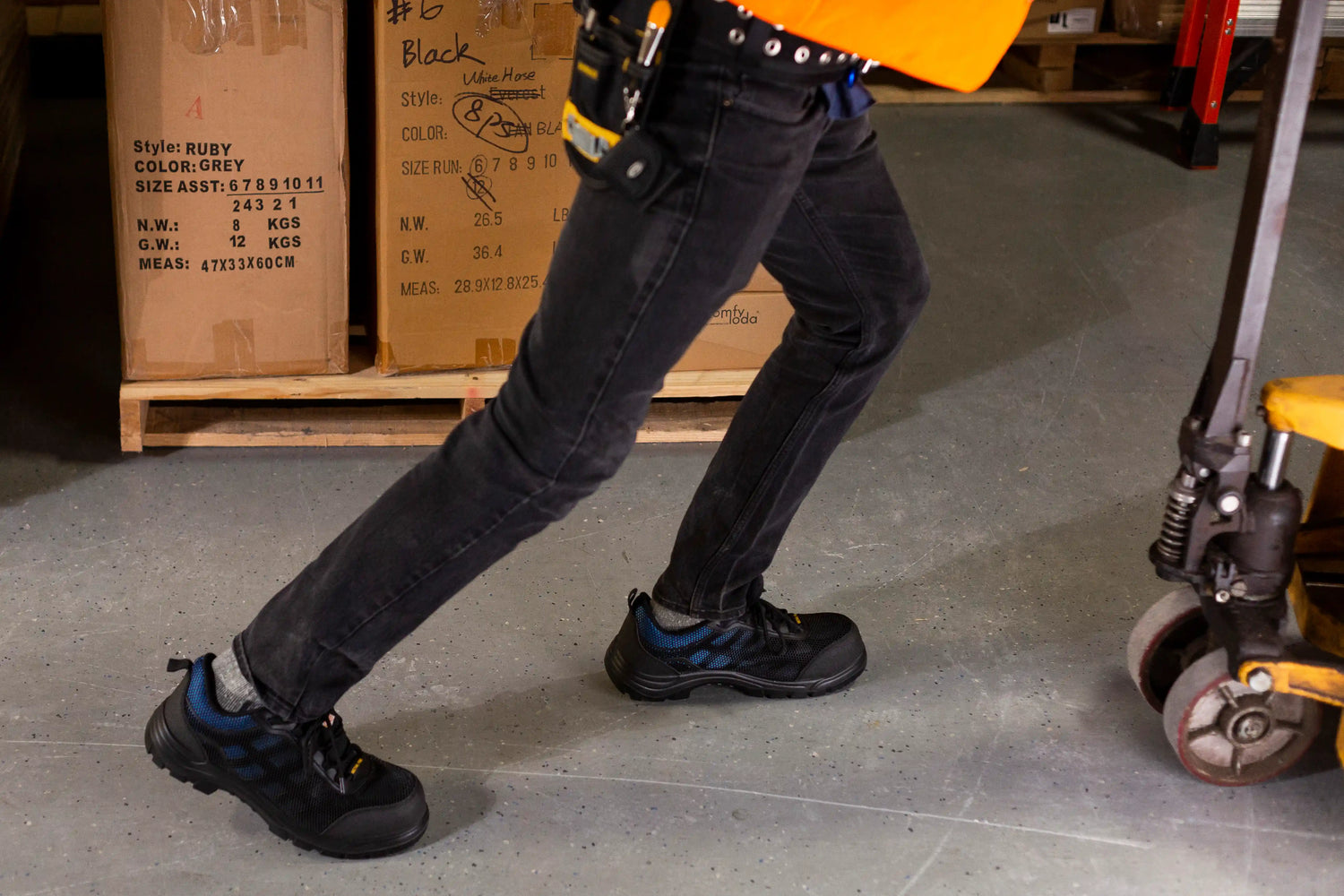 Person wearing black jeans and work shoes in a warehouse setting