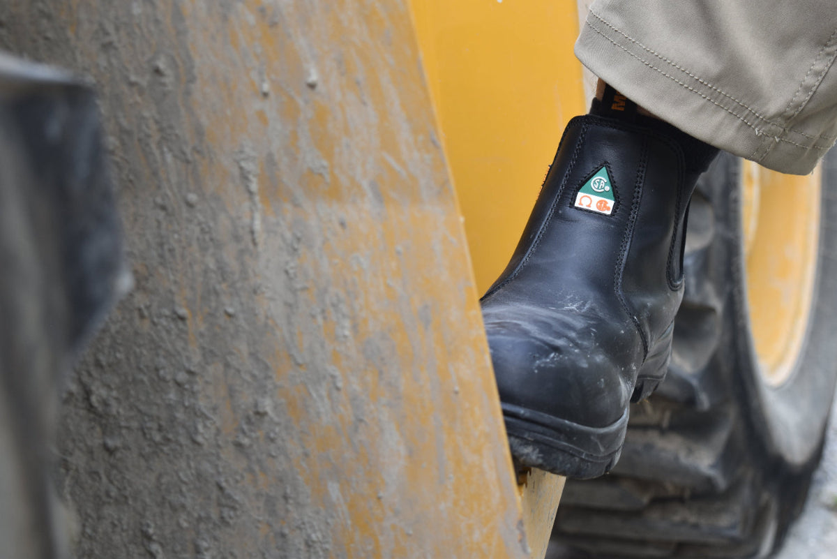 Black work boot with a visible brand logo on a yellow tire background