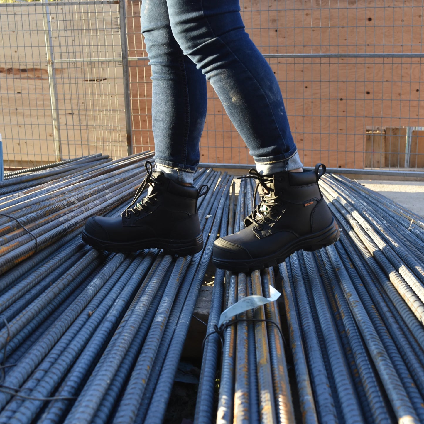 Person wearing black boots and blue jeans standing on metal rebar.