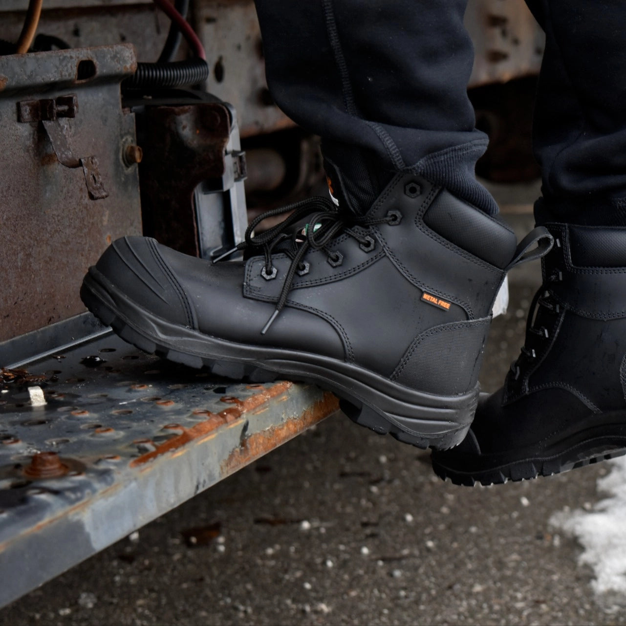 Person wearing gray work boots on a metal surface with a rusty background