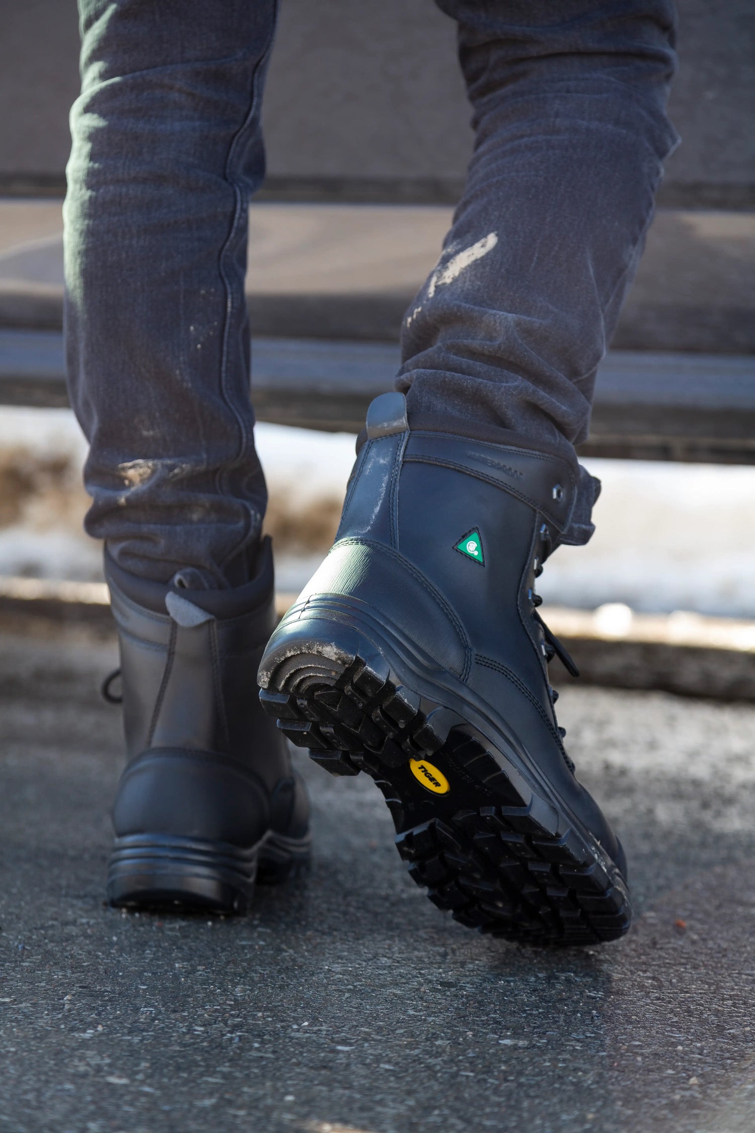 Person wearing black steel toe boots with a yellow sole on a concrete surface