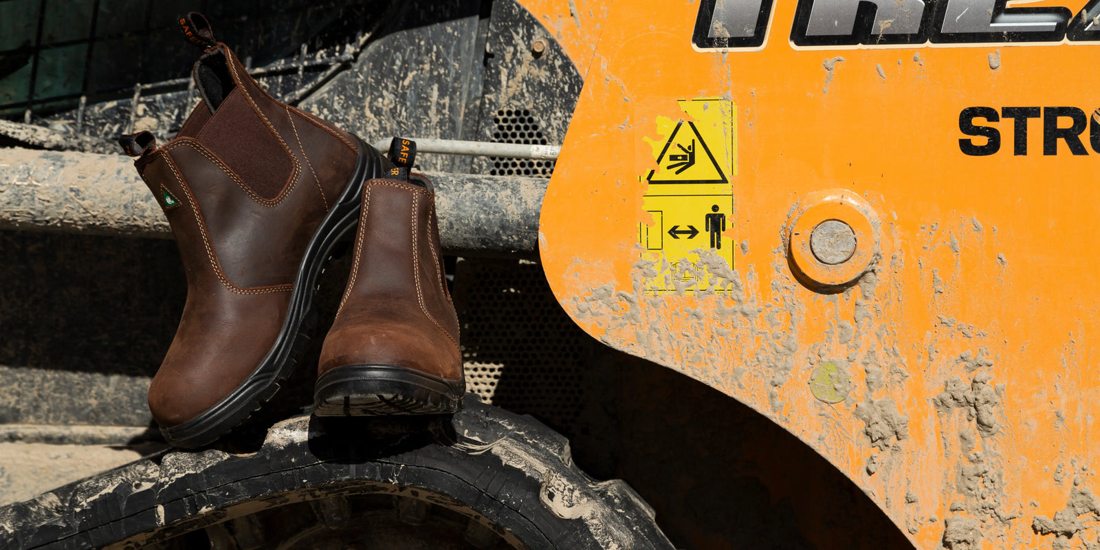 Brown steel toe boots on a piece of heavy machinery with warning labels.